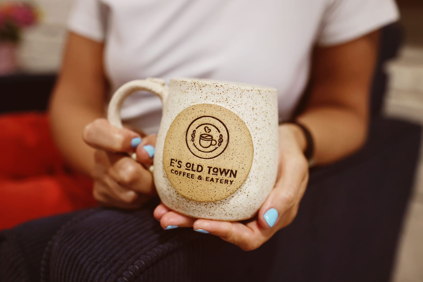 A speckled ceramic E's Old Town mug engraved with the logo, held in two hands